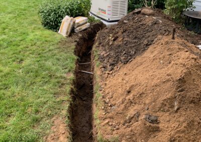 A trench dug in the grass next to a house, possibly for drainage or utility purposes.